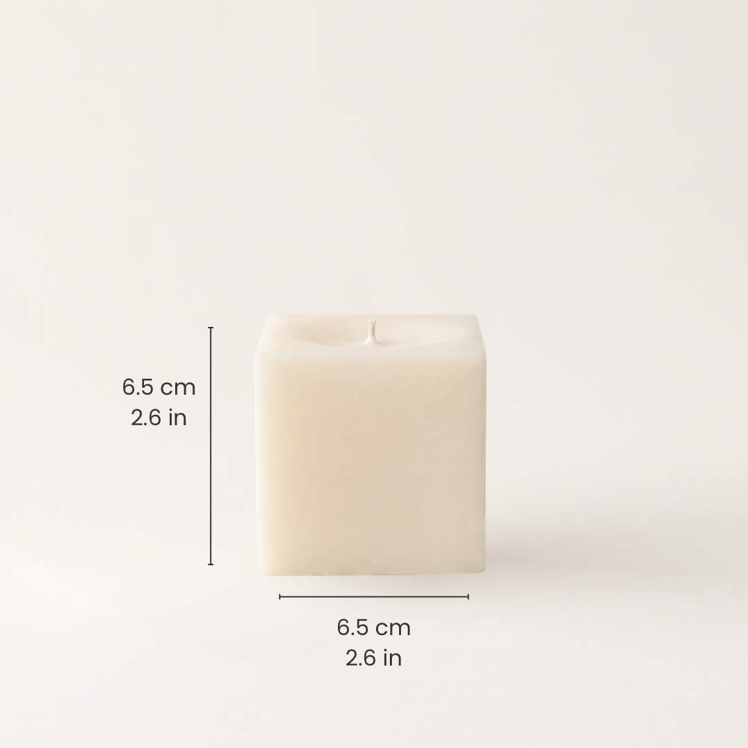 A square cream-colored candle with shown on a light beige background with black dimension lines and text indicating a height and width of 6.5 cm (2.