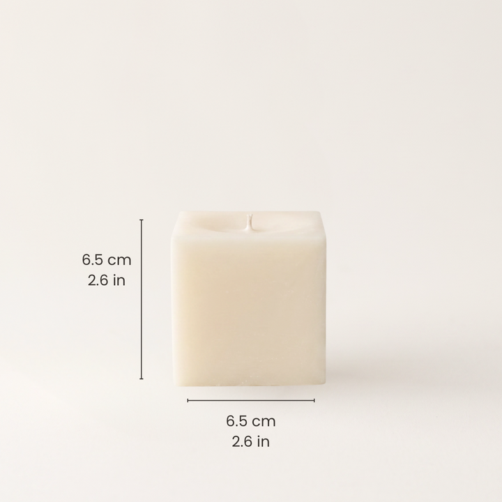 A square cream-colored candle with shown on a light beige background with black dimension lines and text indicating a height and width of 6.5 cm (2.