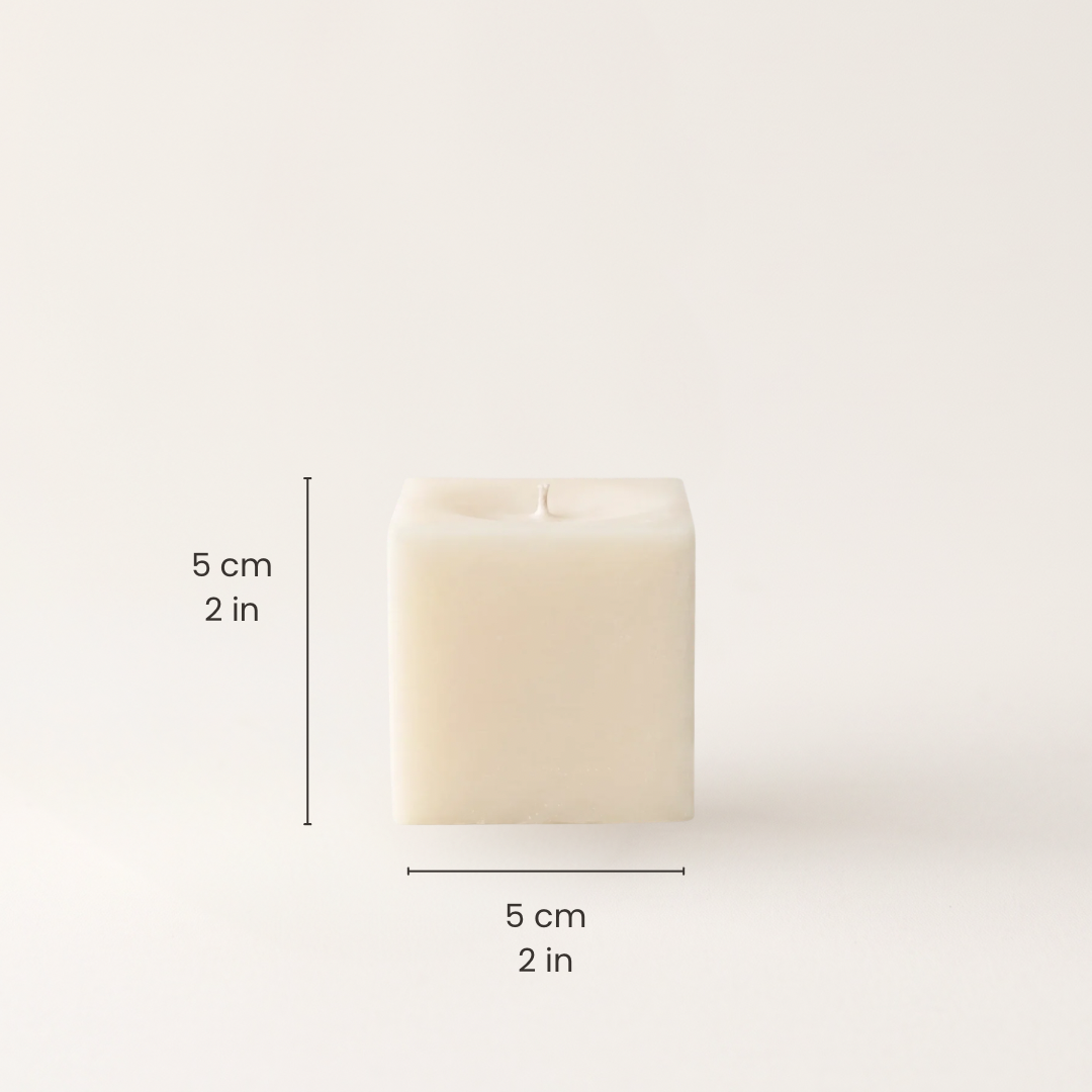 A square cream-colored candle shown on a plain light background with black dimension lines and text indicating 5 cm by 5 cm by 2 in height, width, and depth.