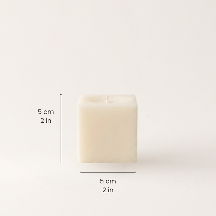 A square cream-colored candle shown on a plain light background with black dimension lines and text indicating 5 cm by 5 cm by 2 in height, width, and depth.