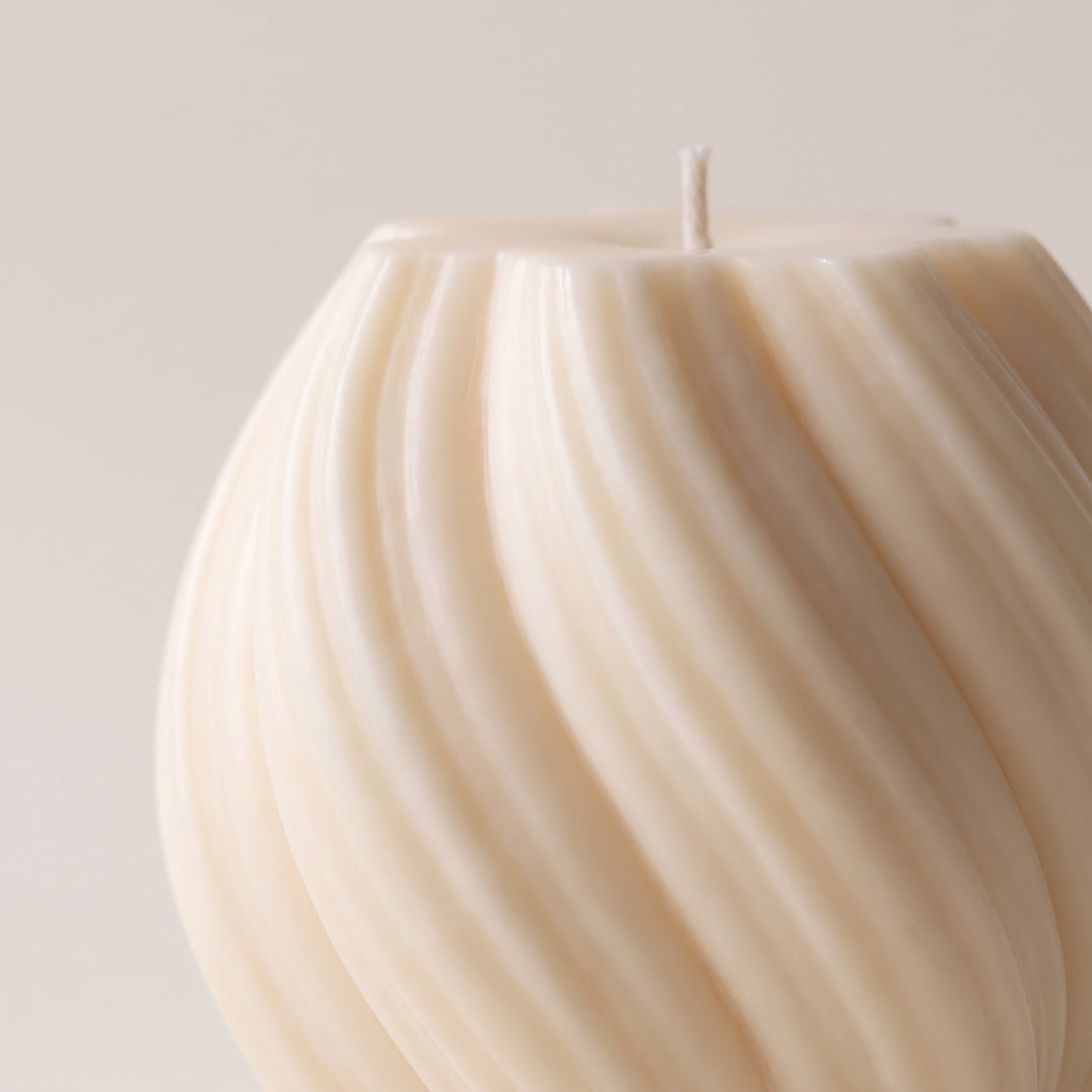 A close-up of a cream-colored spiral ribbed candle with a single wick, set against a solid light beige background.