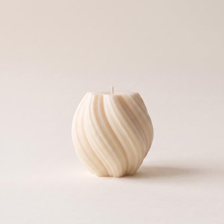 An off-white textured candle with a ribbed, spiral pattern, standing upright on a neutral cream background.