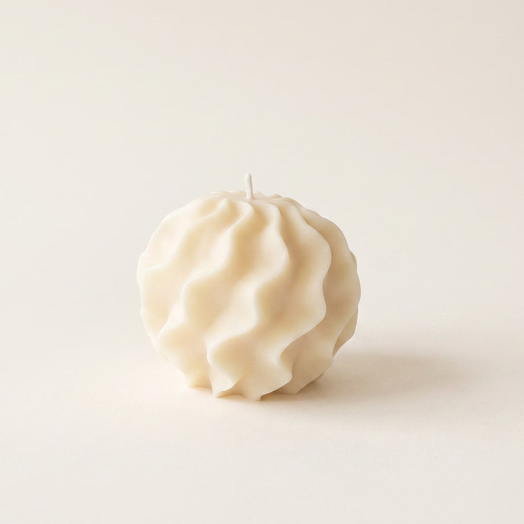 A single cream-colored textured candle with a sculpted, pleated surface and a small wick, centered against a solid, warm off-white background.