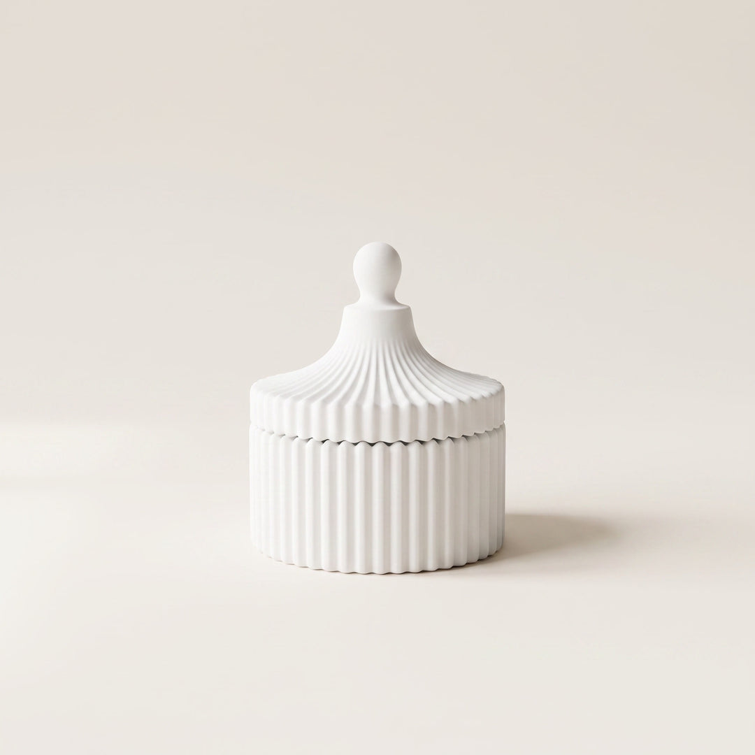 A small white ribbed ceramic lidded box with a rounded knob top, photographed on a clean warm off-white background.
