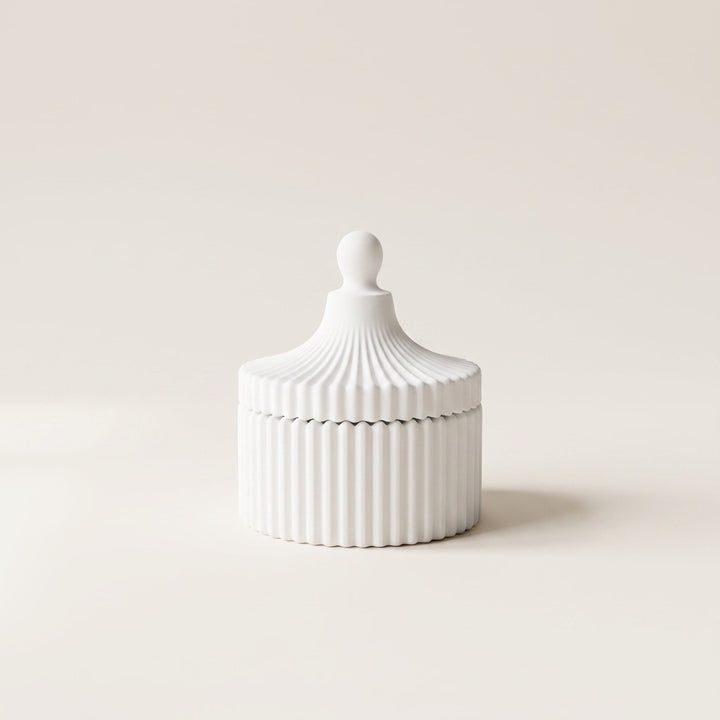 A small white ribbed ceramic lidded box with a rounded knob top, photographed on a clean warm off-white background.
