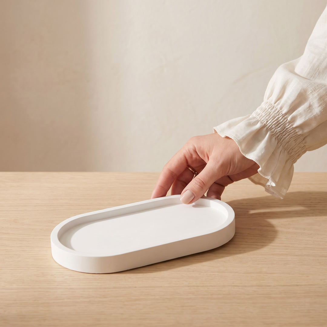 A white oval tray with a raised rim sits on a light wood table, with a person&